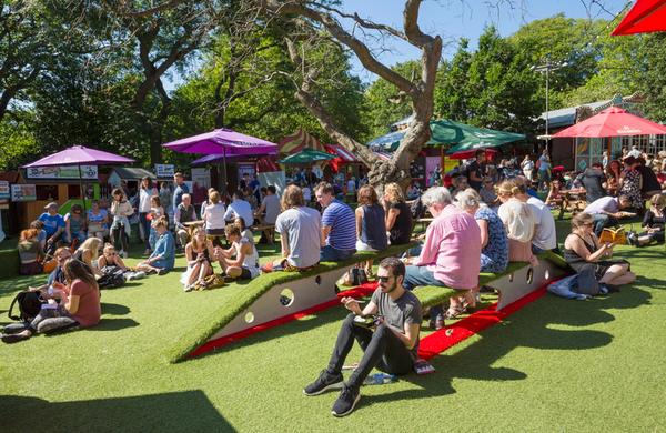 Festival goers sit in the sun at Bristow Square, surrounded by colourful sun parasols and food and drink stalls